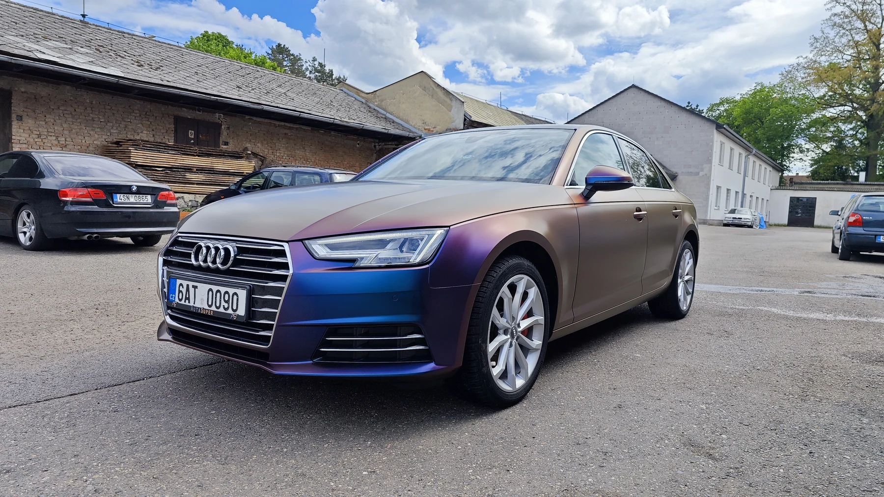Audi A4 v barevně proměnlivém fialovomodrém celopolepu zepředu a z boku před dílnou
