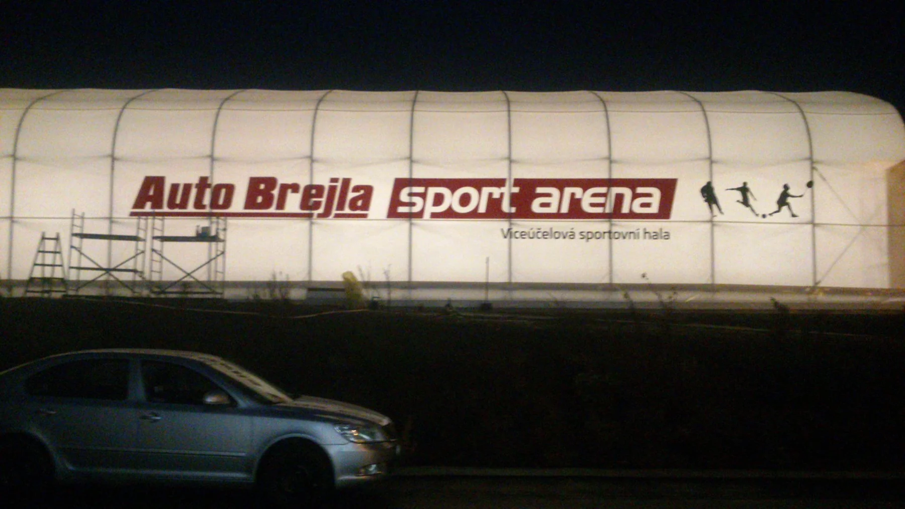 Bílá sportovní hala s velkým červeným nápisem Auto Brejla sportarena večer