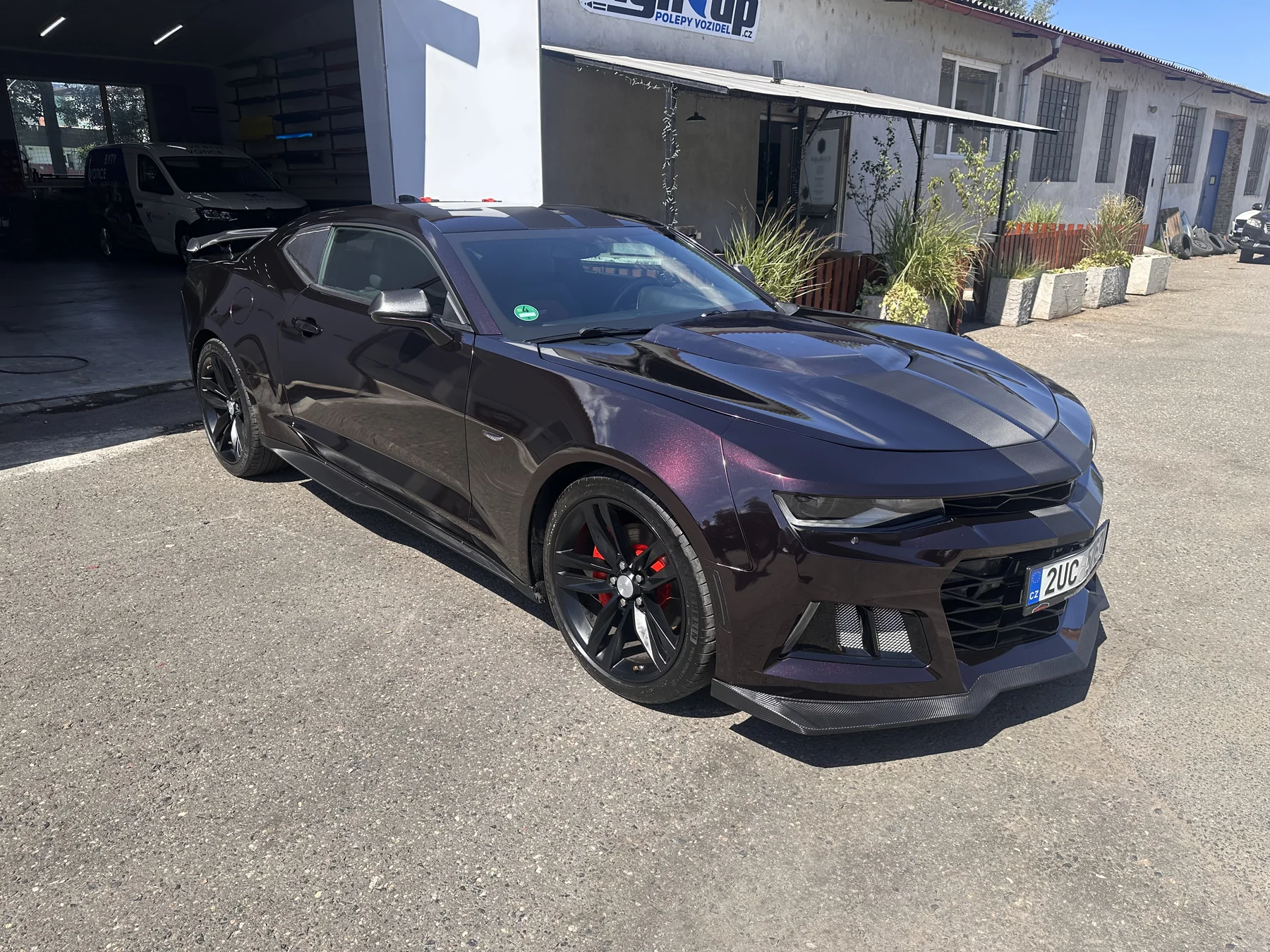 Chevrolet Camaro s tmavě fialovým polepem před dílnou v pohledu zepředu a z boku