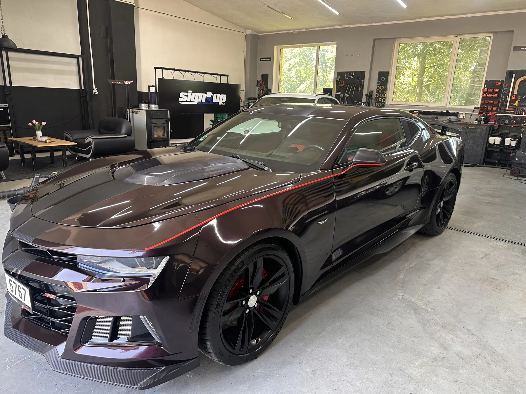 Chevrolet Camaro v dílně s tmavým polepem a červenou linkou na předním blatníku