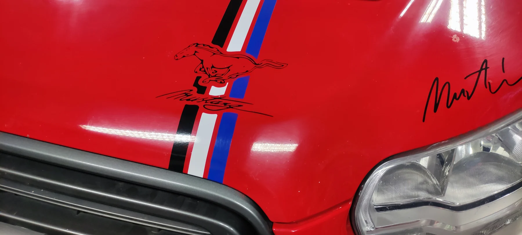 Detail grafiky a tříbarevného pruhu na kapotě červeného Fordu