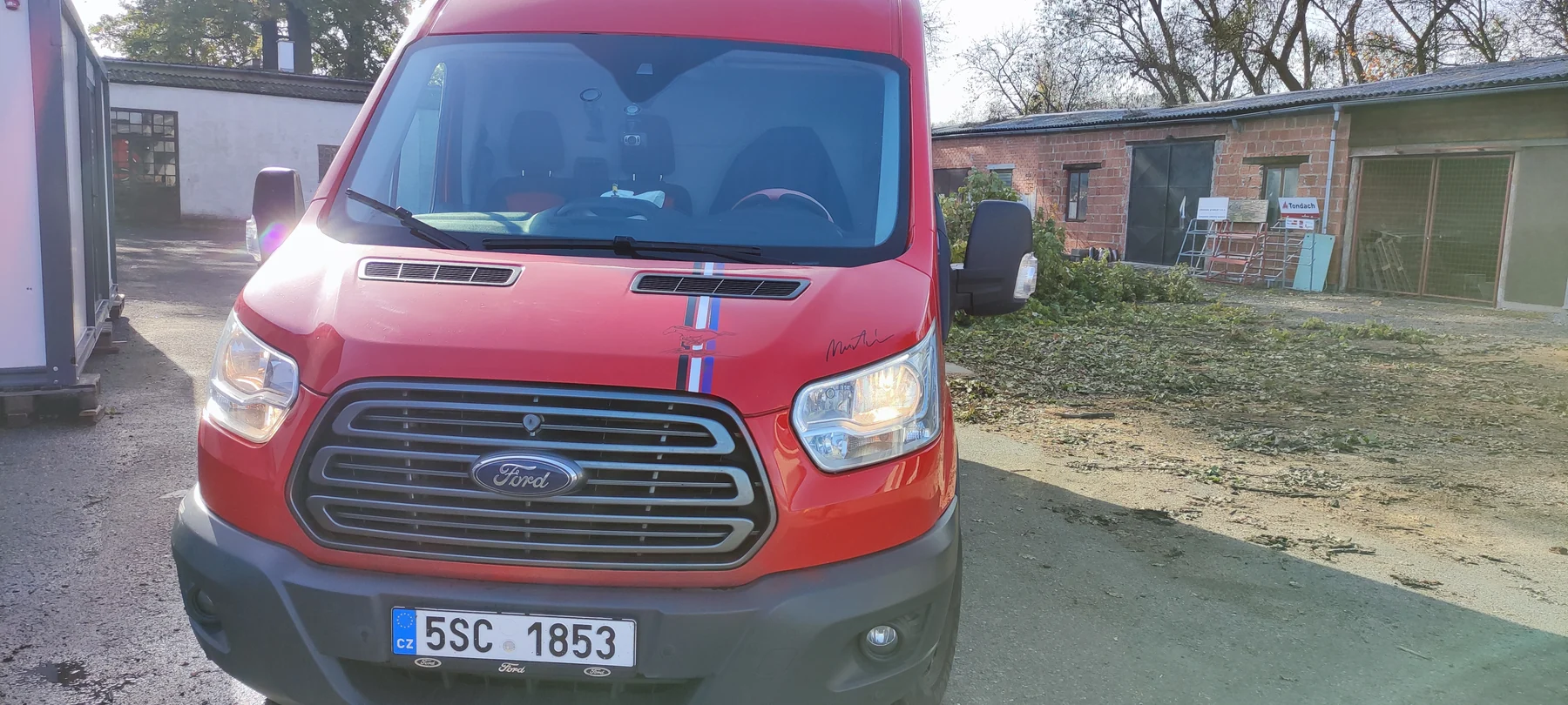Přední část červené dodávky Ford s úzkými barevnými pruhy na kapotě
