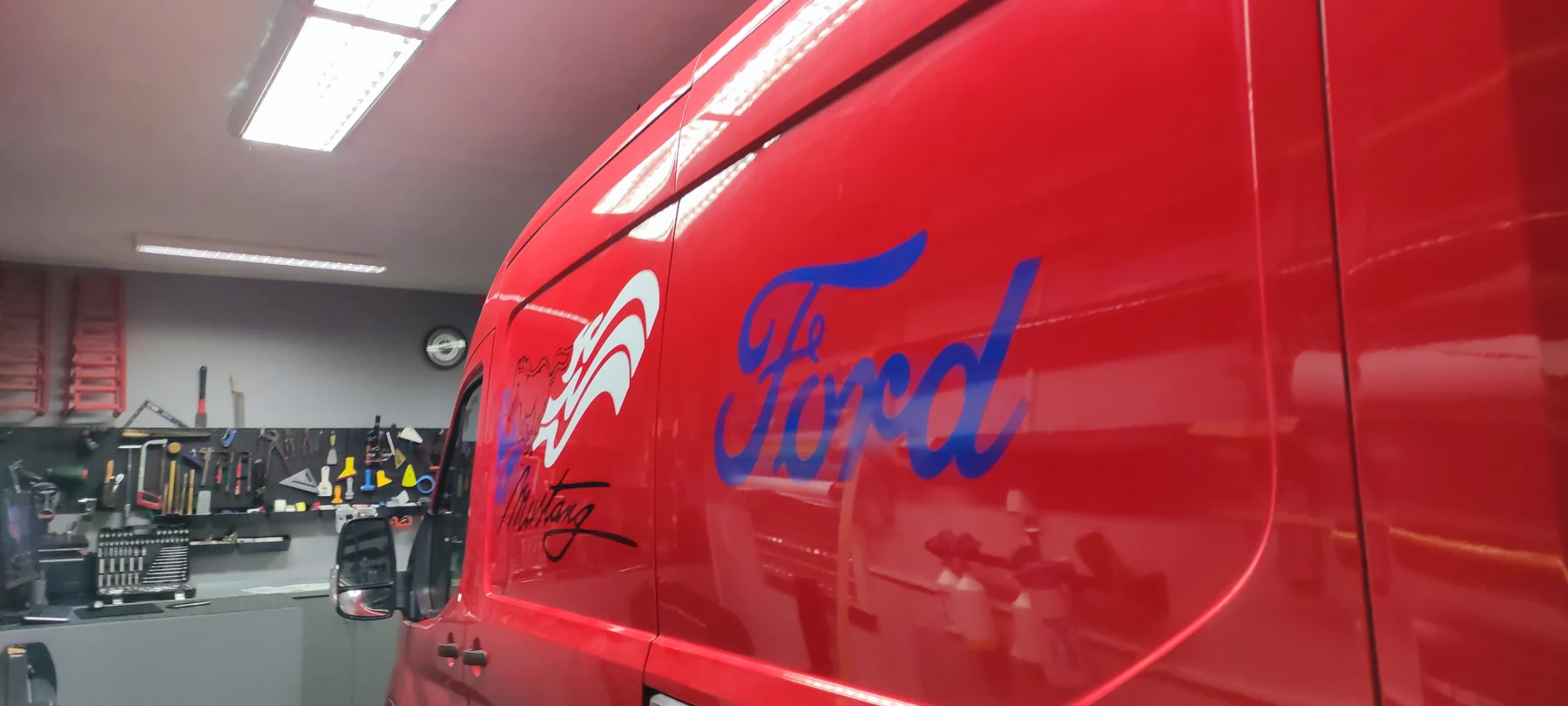 Detail bílého motivu a modrého nápisu Ford na červeném boku dodávky
