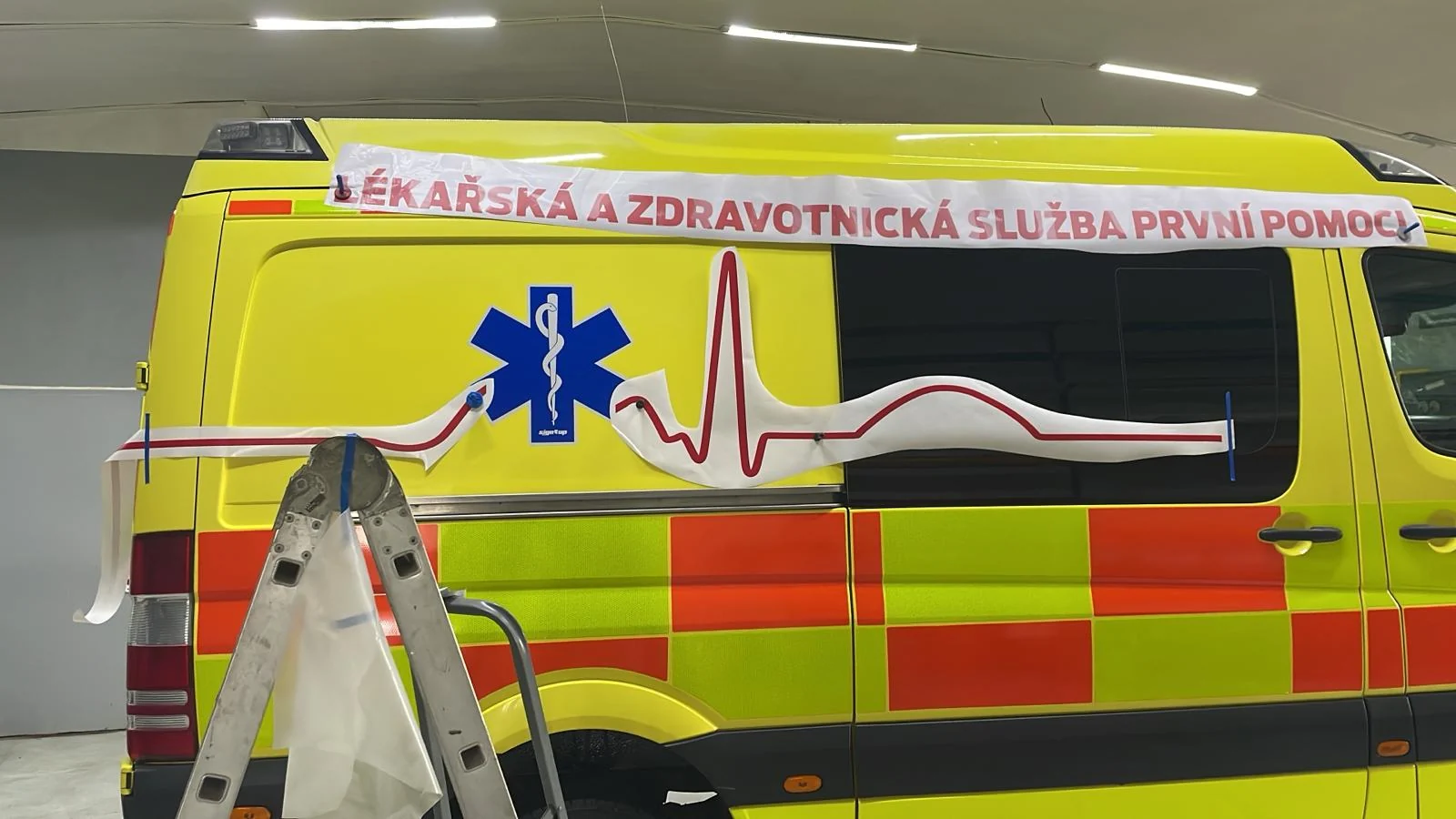Příprava červené linky a nápisu na boku sanitky při aplikaci