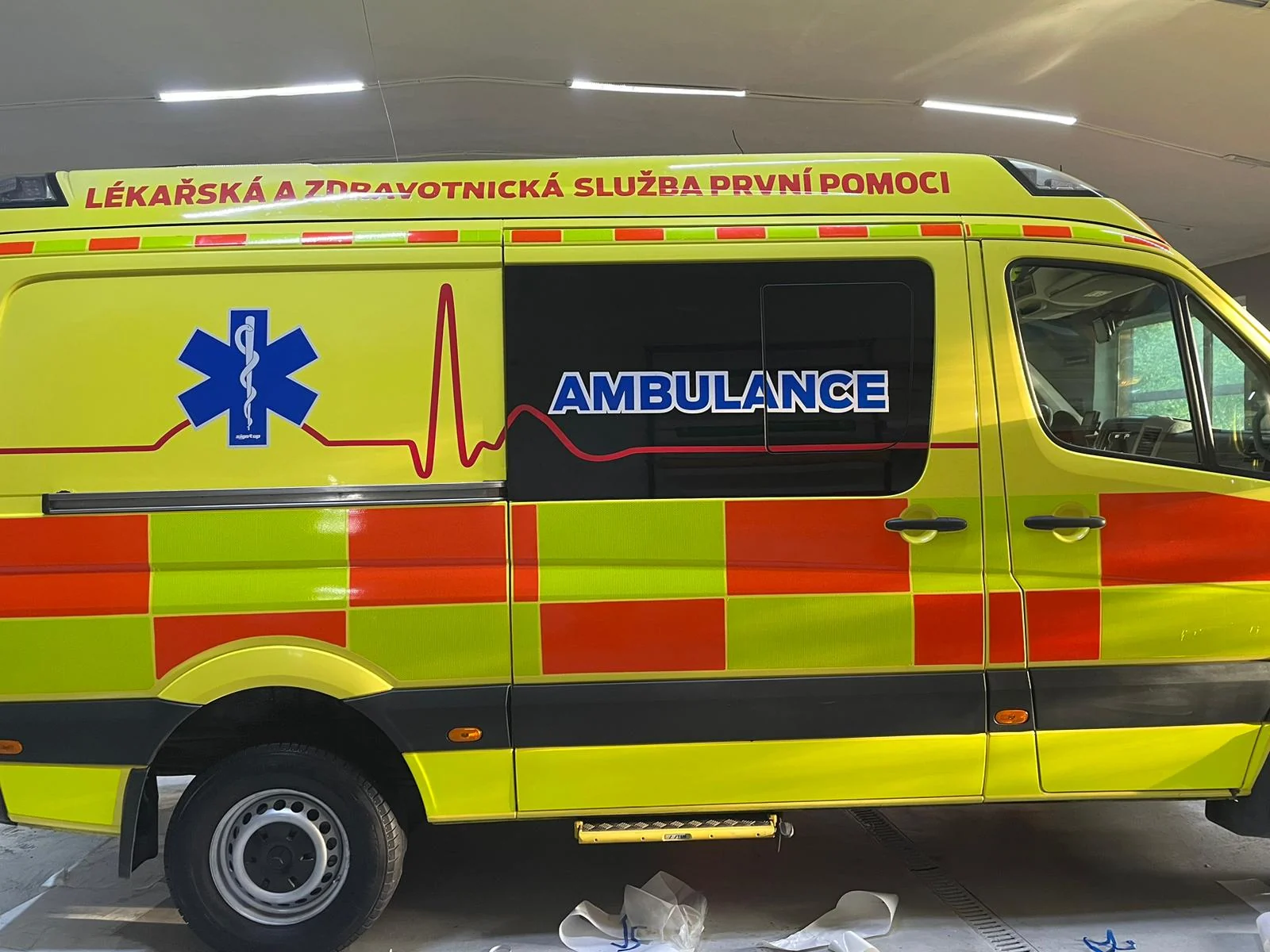 Detail boku sanitky s modrou hvězdou, nápisem Ambulance a červenou linkou