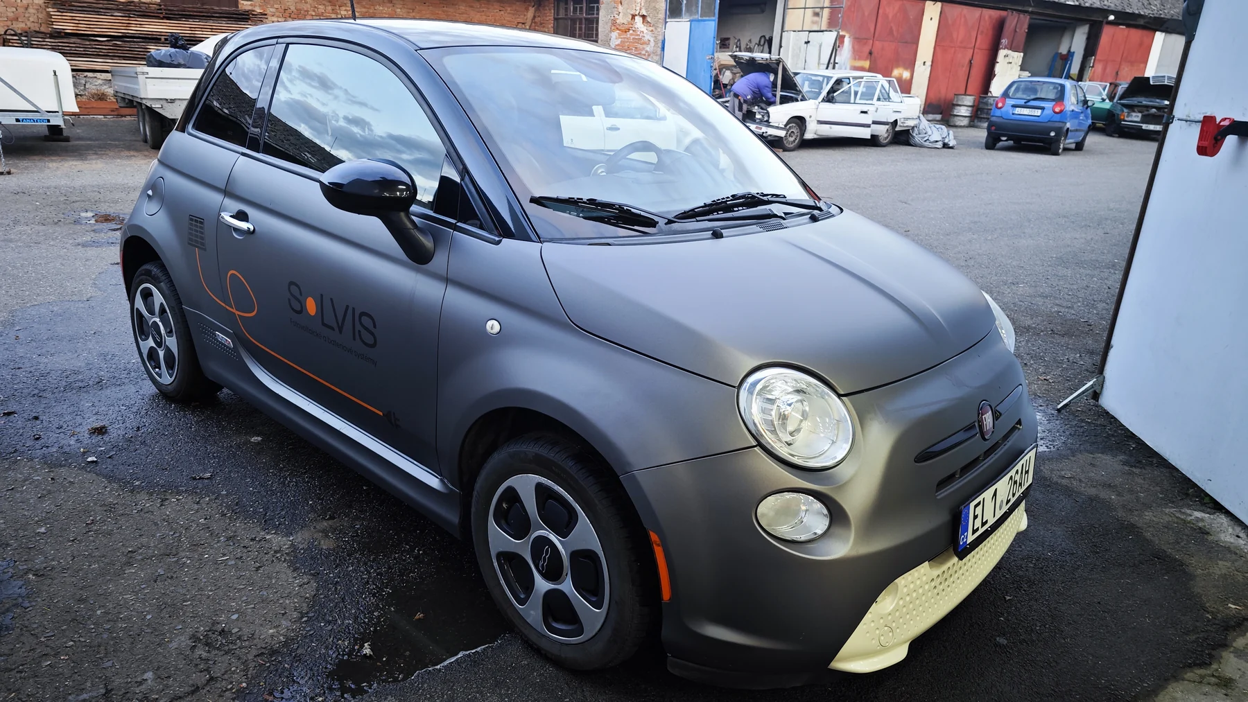 Šedý Fiat 500 s oranžovým reklamním polepem SOLVIS zepředu a z boku