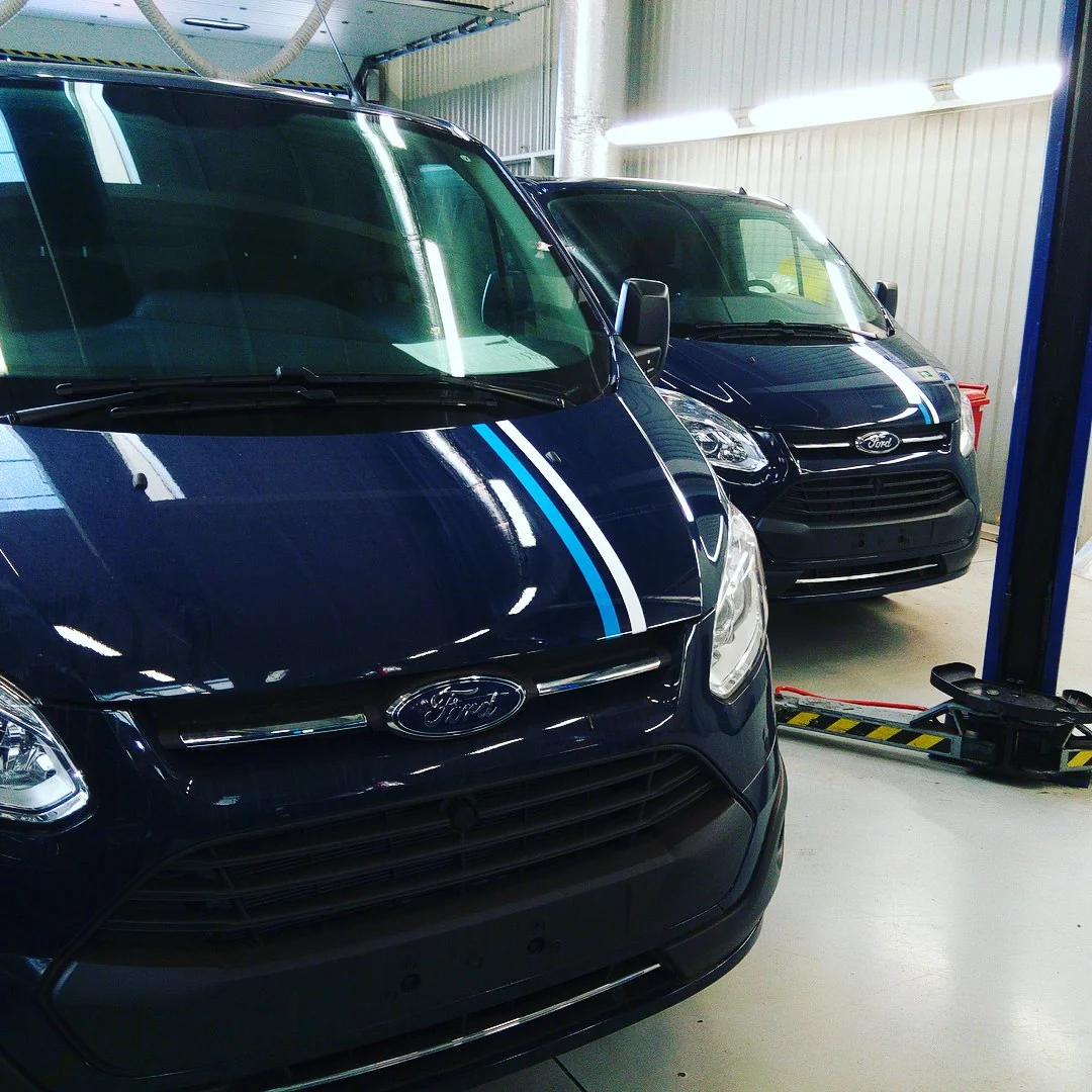 Detail světle modré a bílé pruhové grafiky na tmavé přídi dodávky Ford