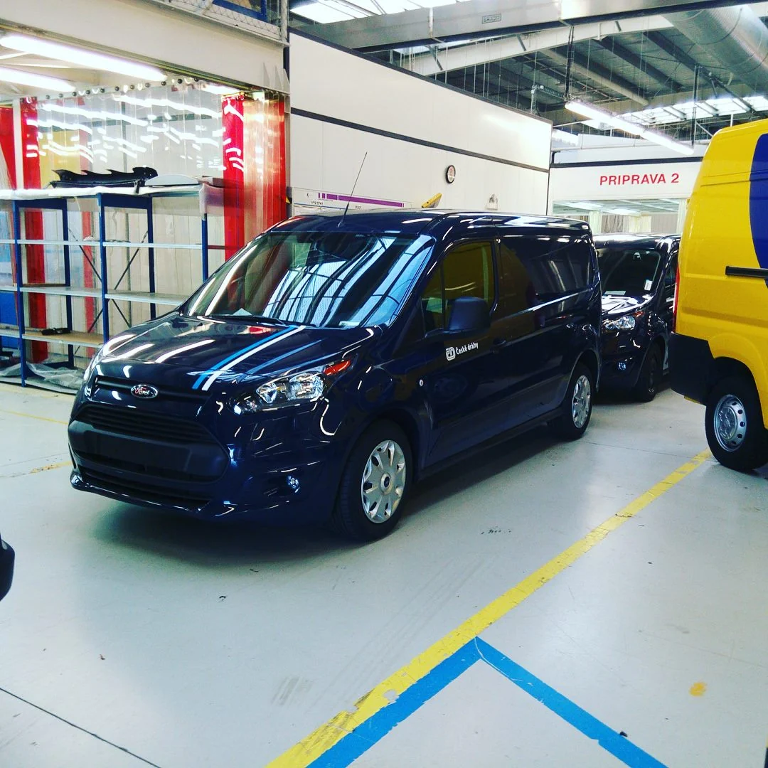 Tmavě modrá dodávka Ford se světle modrými a bílými sportovními pruhy