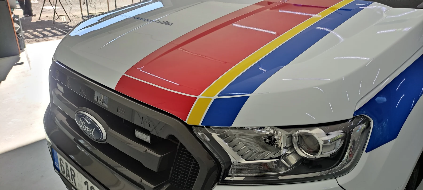 Detail červenožlutého šikmého značení na kapotě Fordu Ranger