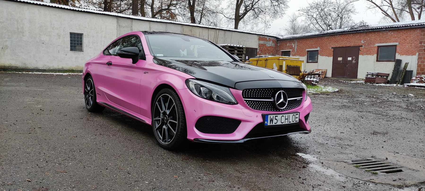 Mercedes kupé v růžovém polepu s černou kapotou, pohled zepředu a z boku před dílnou