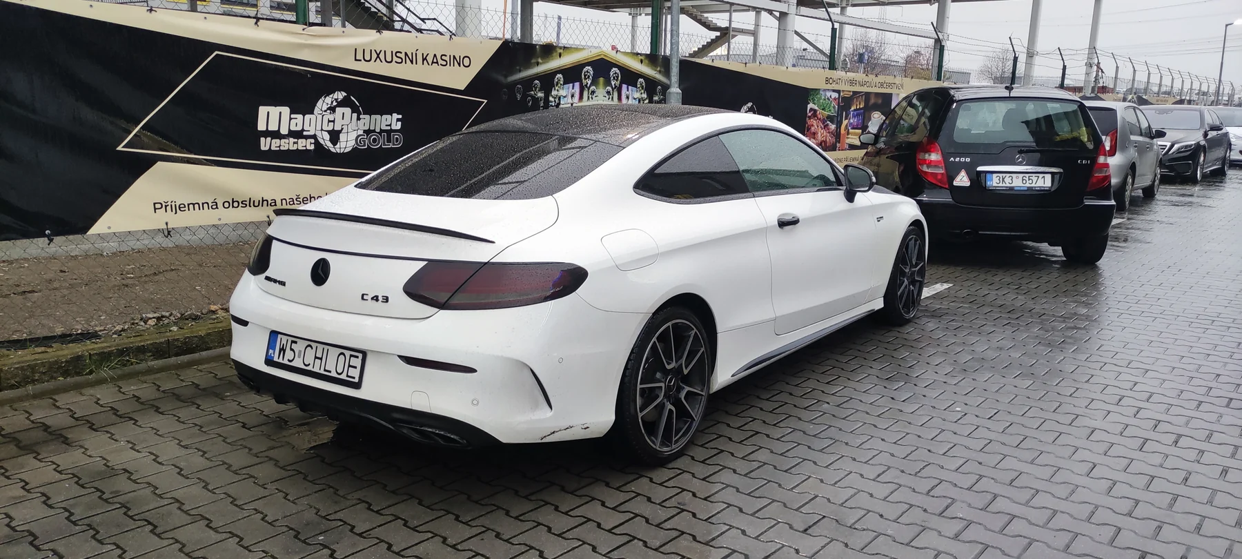 Stejný Mercedes kupé v bílém provedení před růžovým polepem, pohled zezadu a z boku
