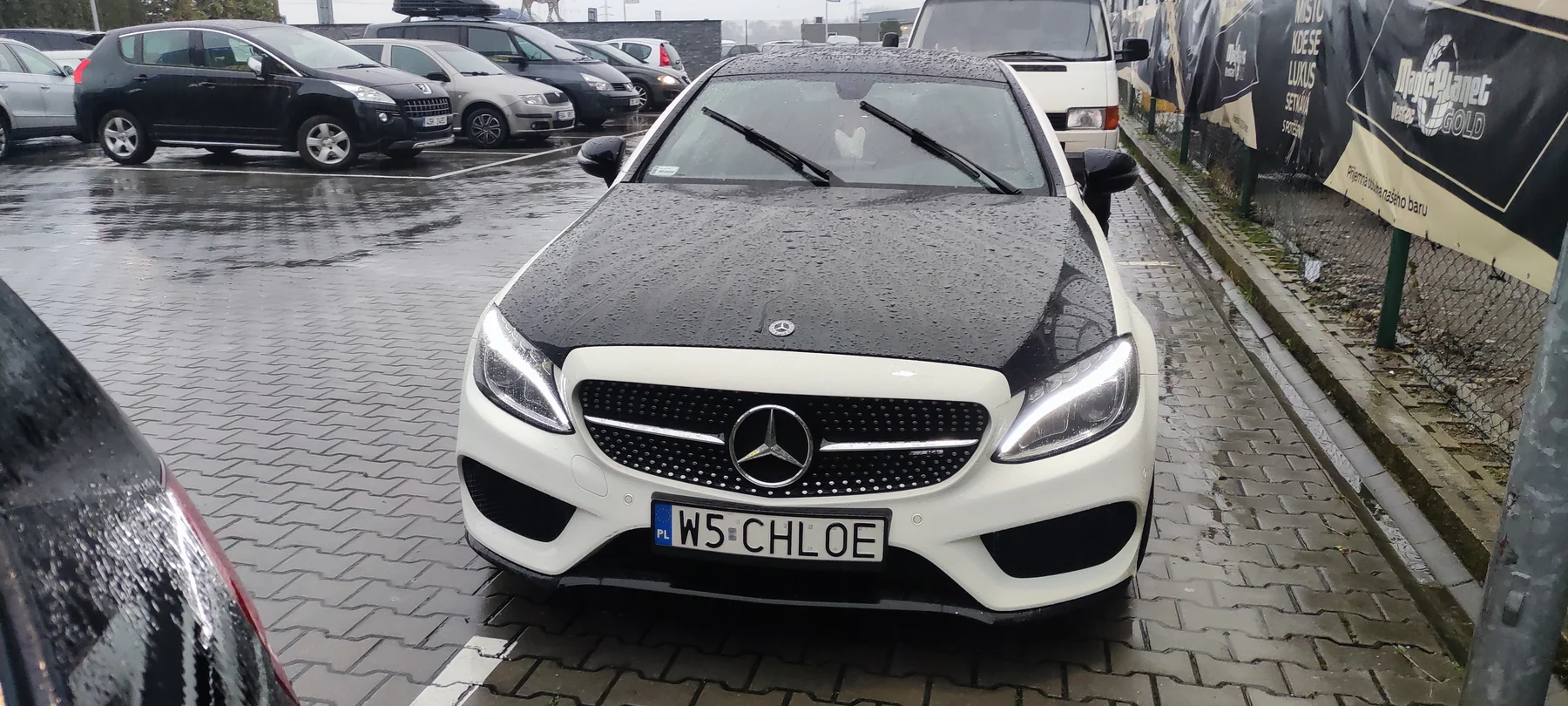 Bílý Mercedes kupé s černou kapotou před růžovým celopolepem zepředu