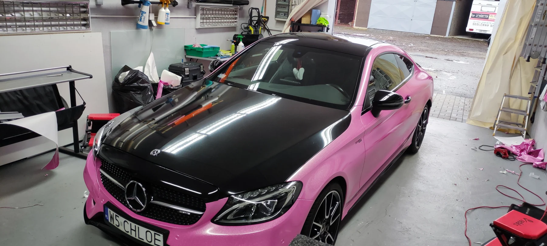 Růžový Mercedes kupé s černou kapotou zachycený shora v dílně