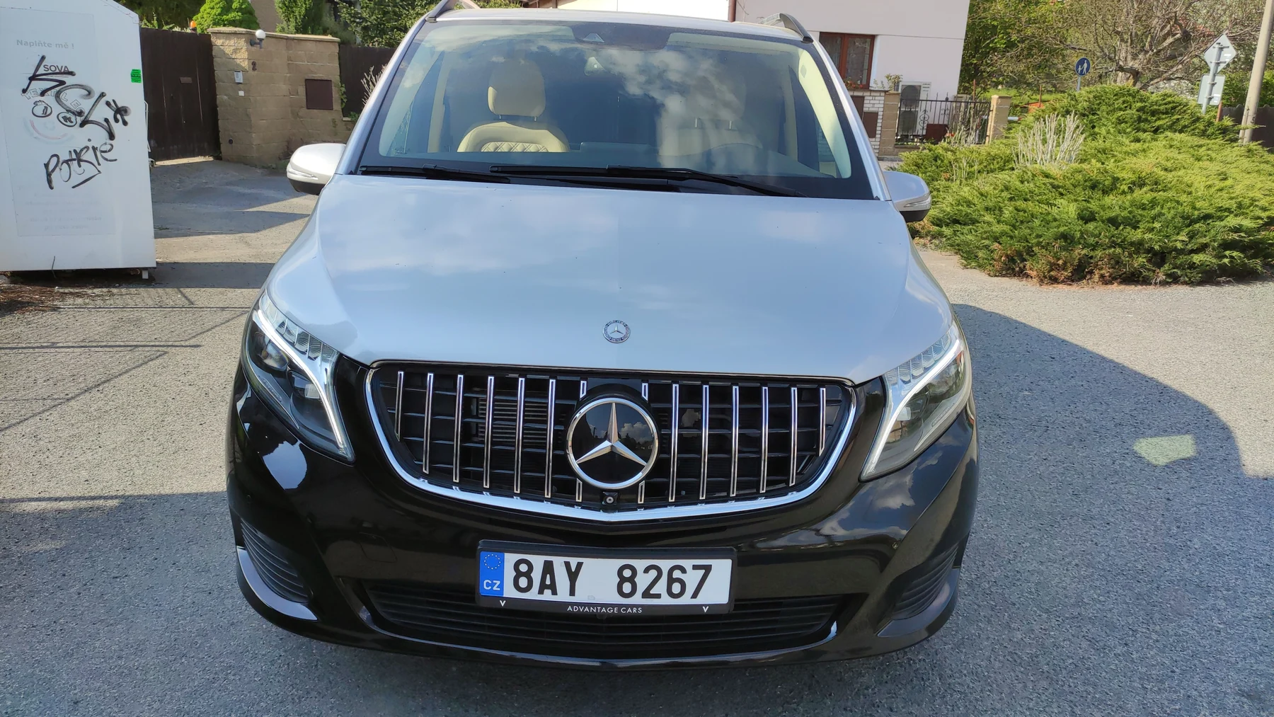 Přední část stříbrnočerného Mercedesu třídy V venku před budovou