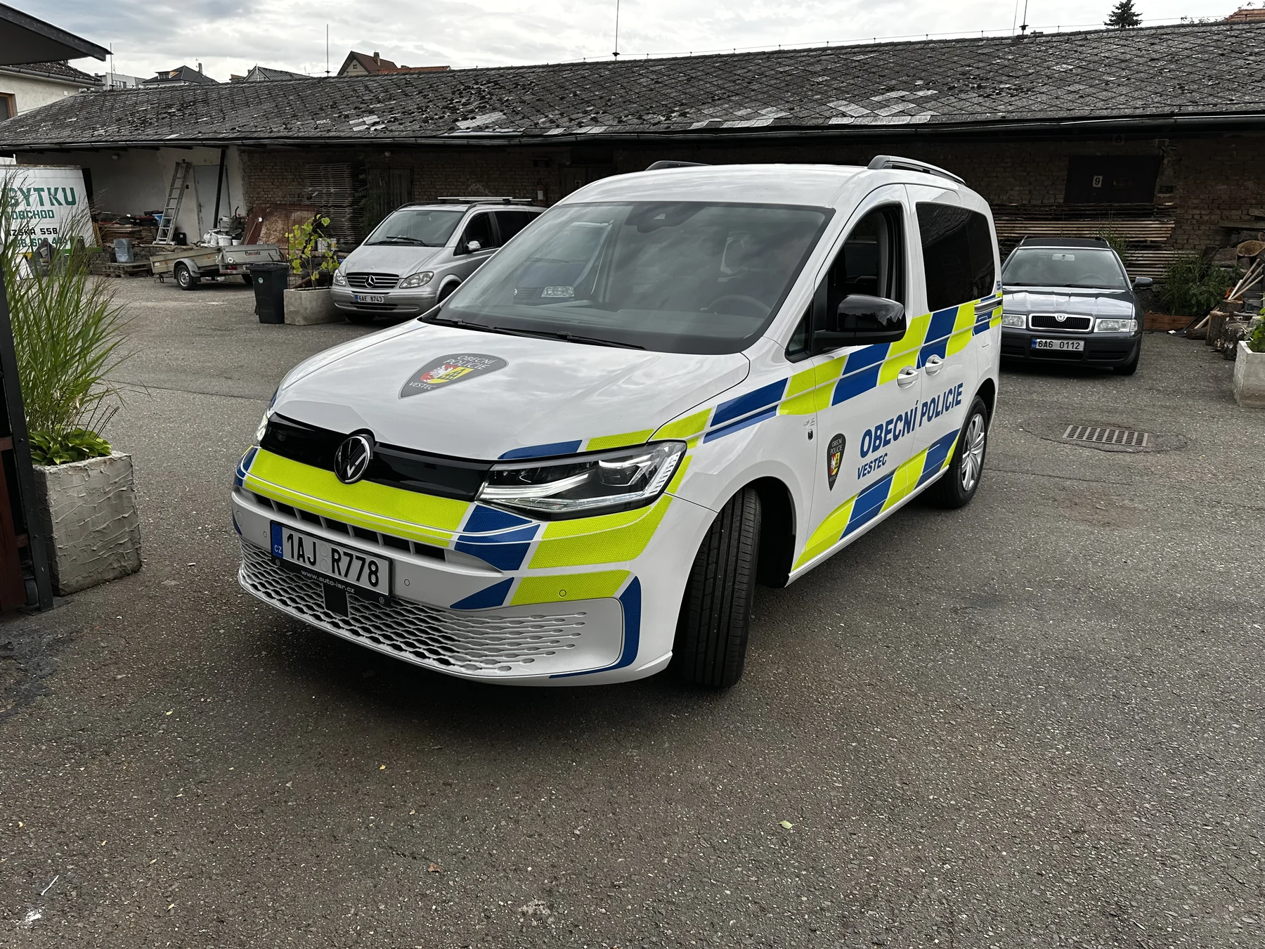 Bílý Volkswagen Caddy Obecní policie Vestec s modrožlutým polepem zepředu a z boku