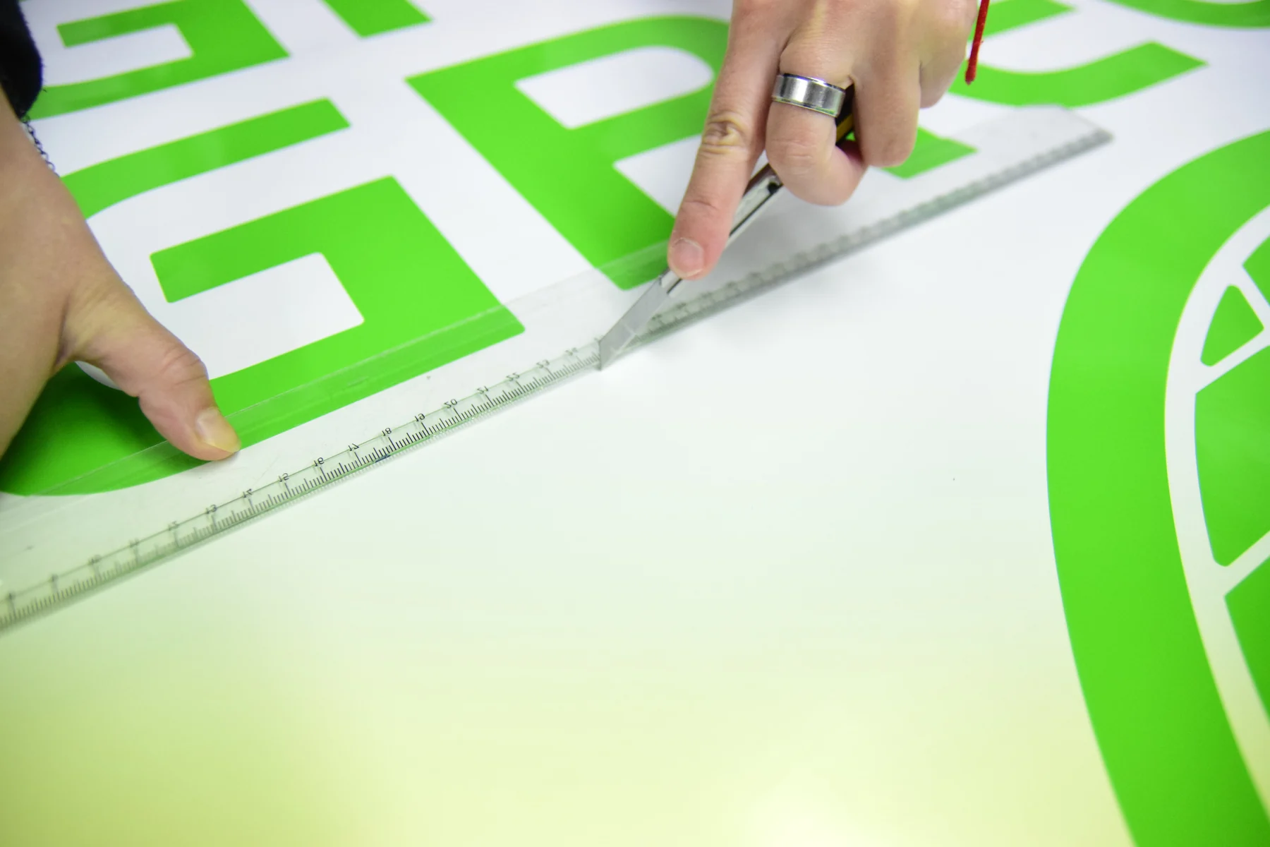 Ruce při dělení grafického podkladu s velkým zeleným logem ELEGreen podle pravítka