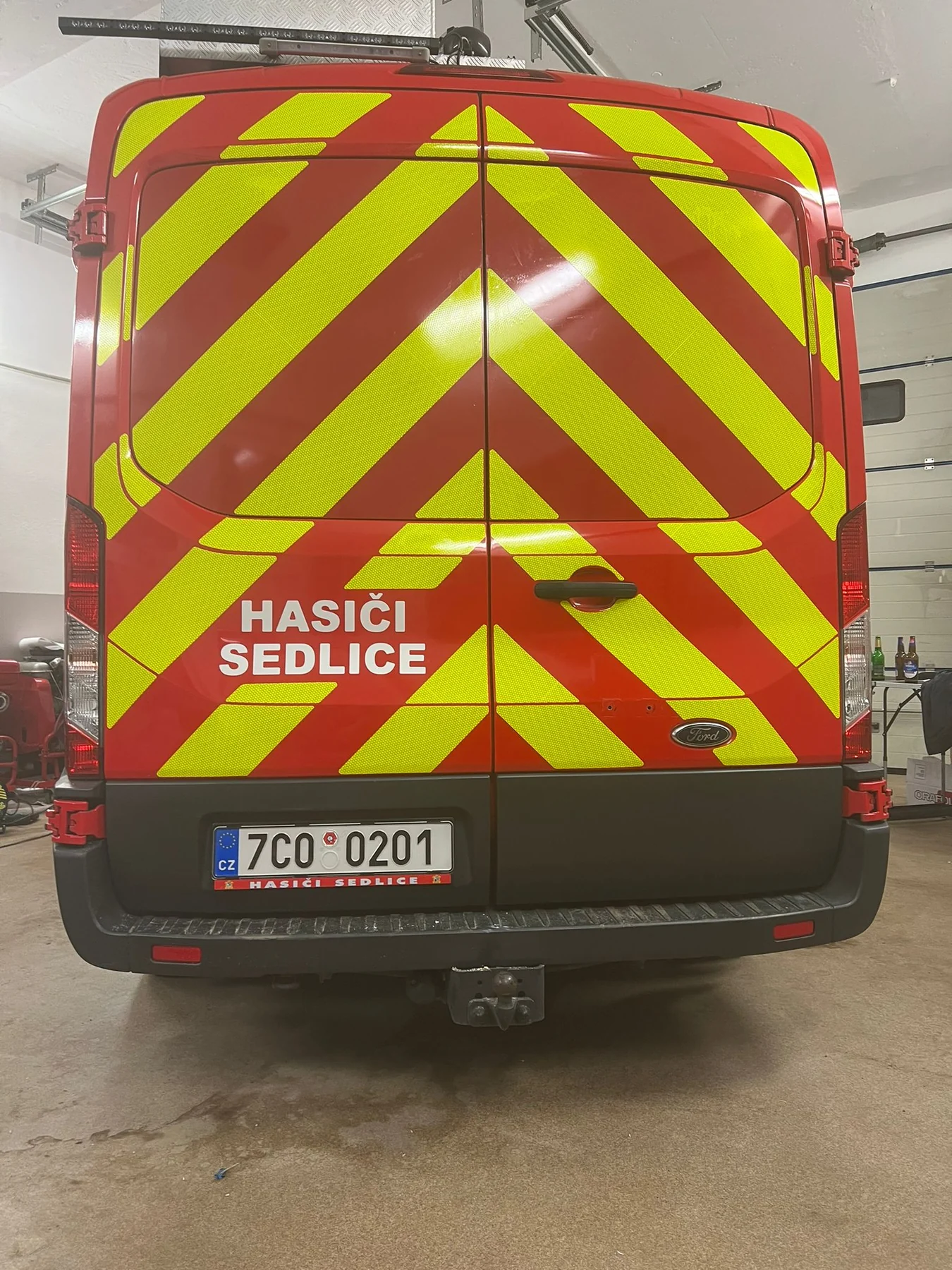 Zadní část červeného Fordu Transit Hasiči Sedlice s hotovým žlutým šrafováním a bílým označením jednotky