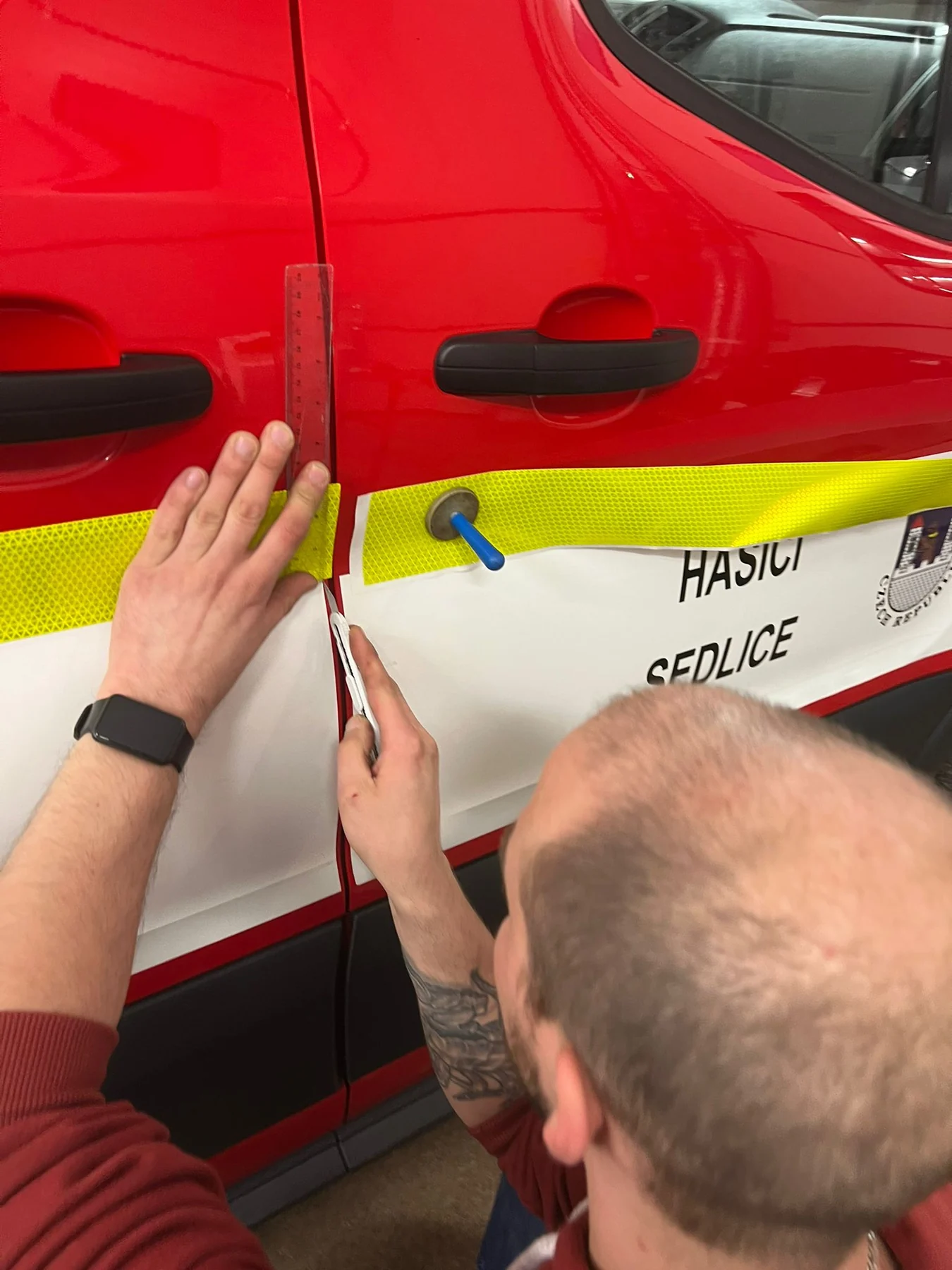Pracovník usazuje žlutý pás na boku Fordu Transit hasičů Sedlice