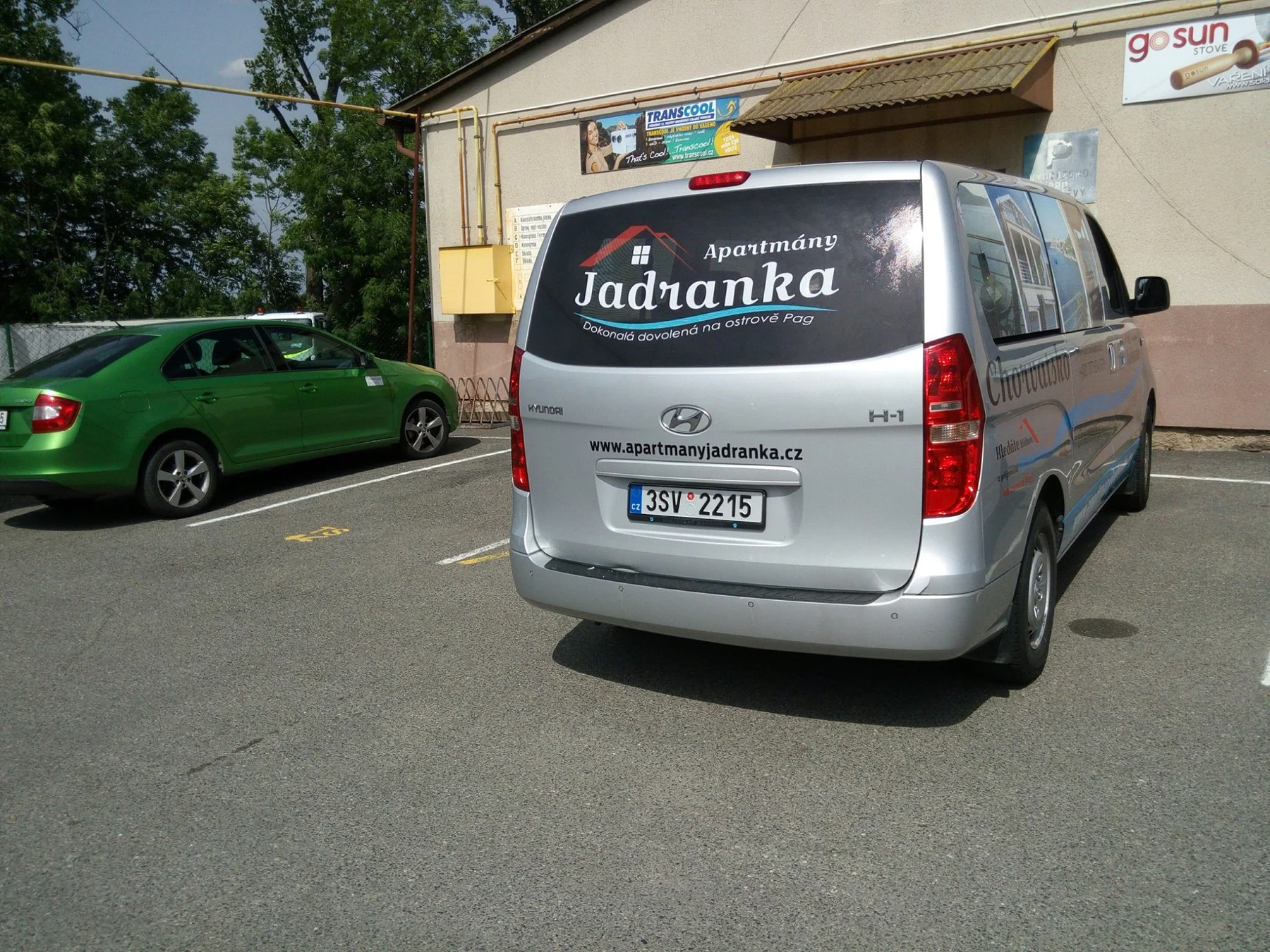 Zadní část stříbrné dodávky s označením Apartmány Jadranka na skle