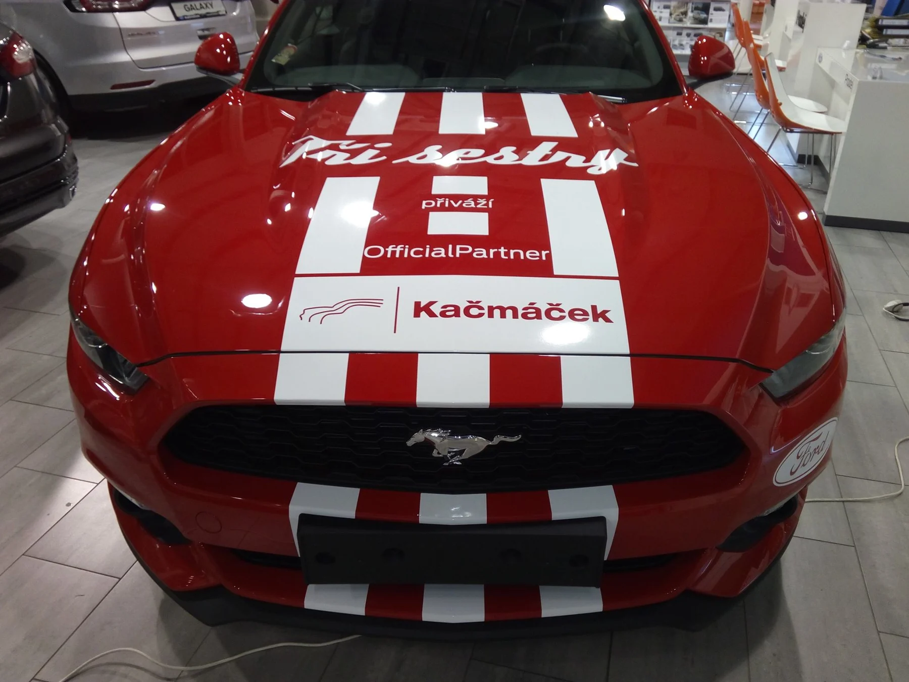 Kapota Mustangu s bílými pruhy, nápisem Tři sestry a dalšími logy