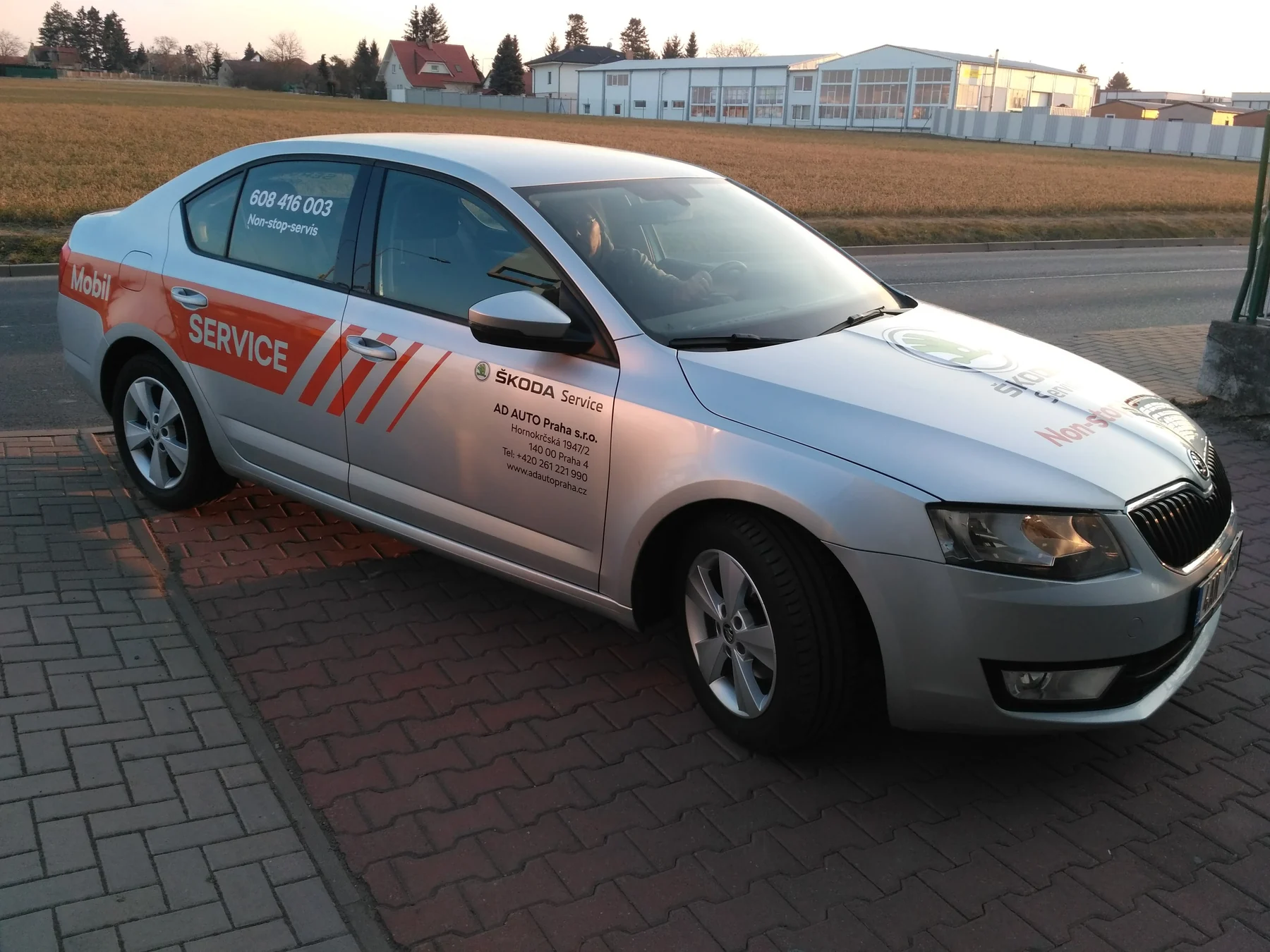 Stříbrný servisní vůz Škoda AD AUTO Praha s oranžovým polepem zepředu a z boku