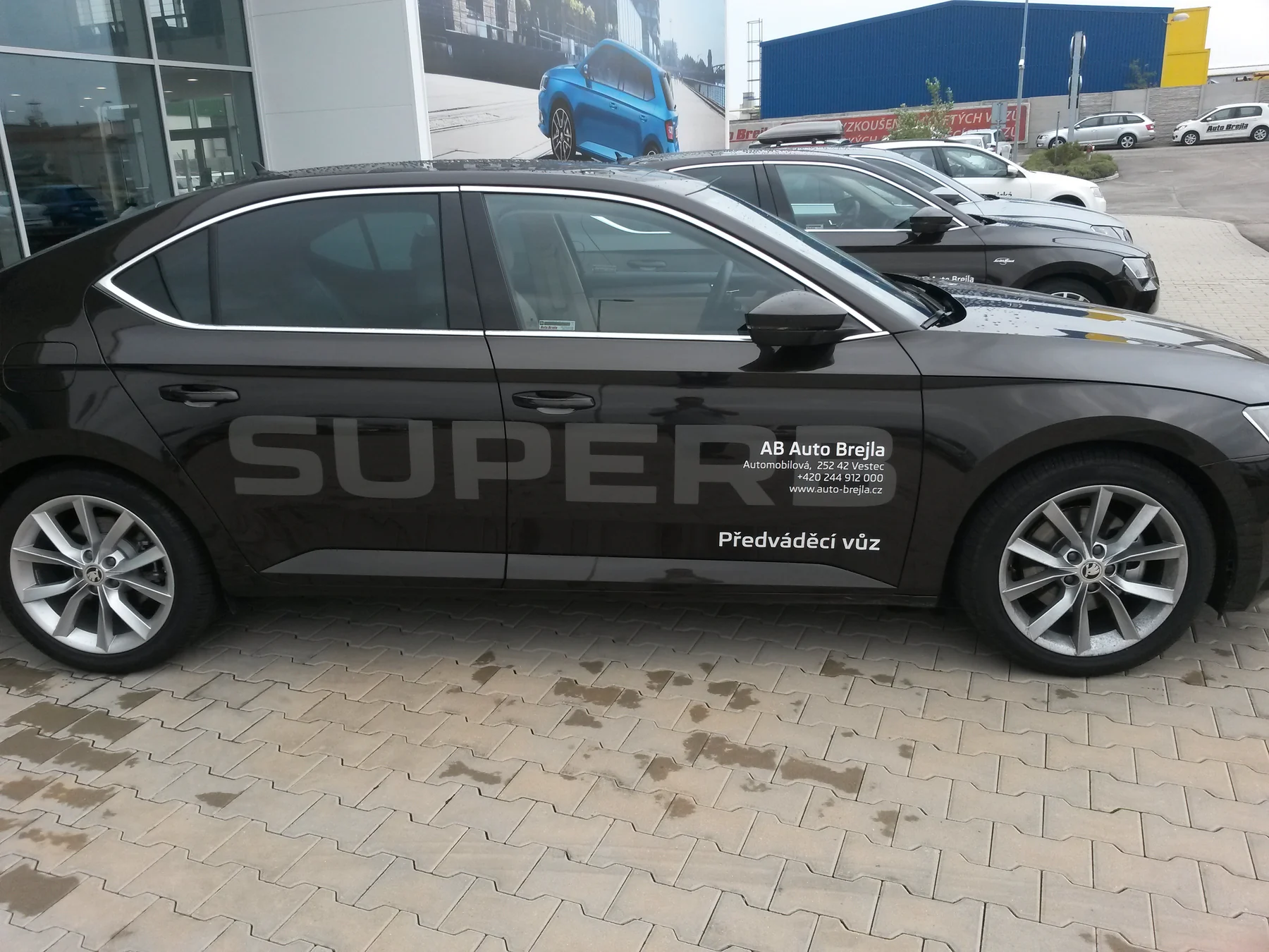 Tmavý Superb na prodejní ploše s reklamním nápisem na boku