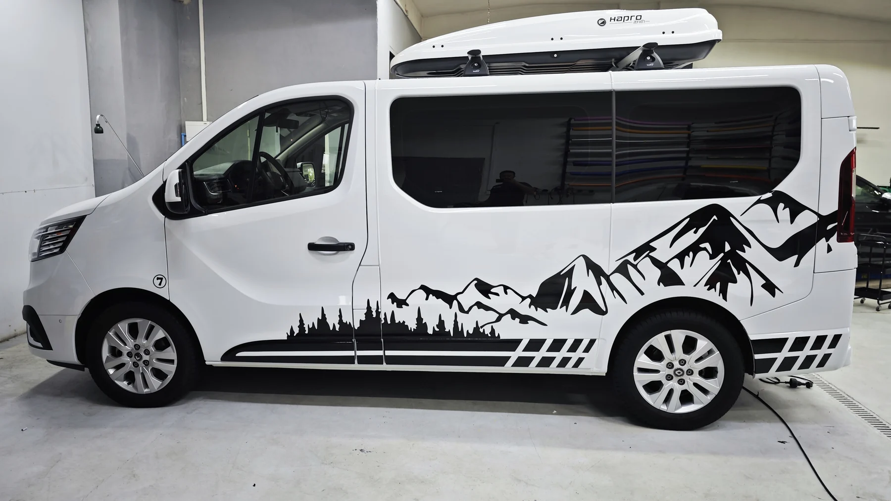 Bílý Renault Trafic s černým polepem hor a lesa přes boční dveře