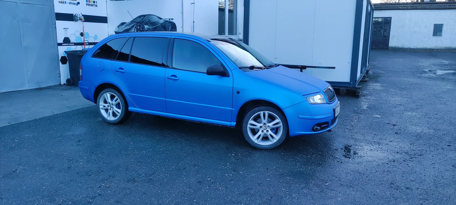 Modrá Fabia kombi s tmavými okny venku před dílnou