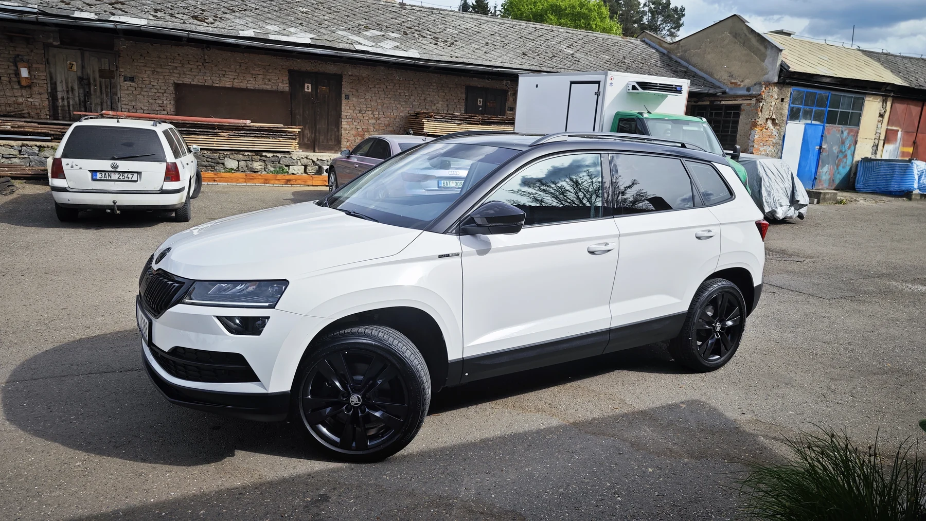 Bílá Škoda Karoq s dokončenou černou střechou před dílnou