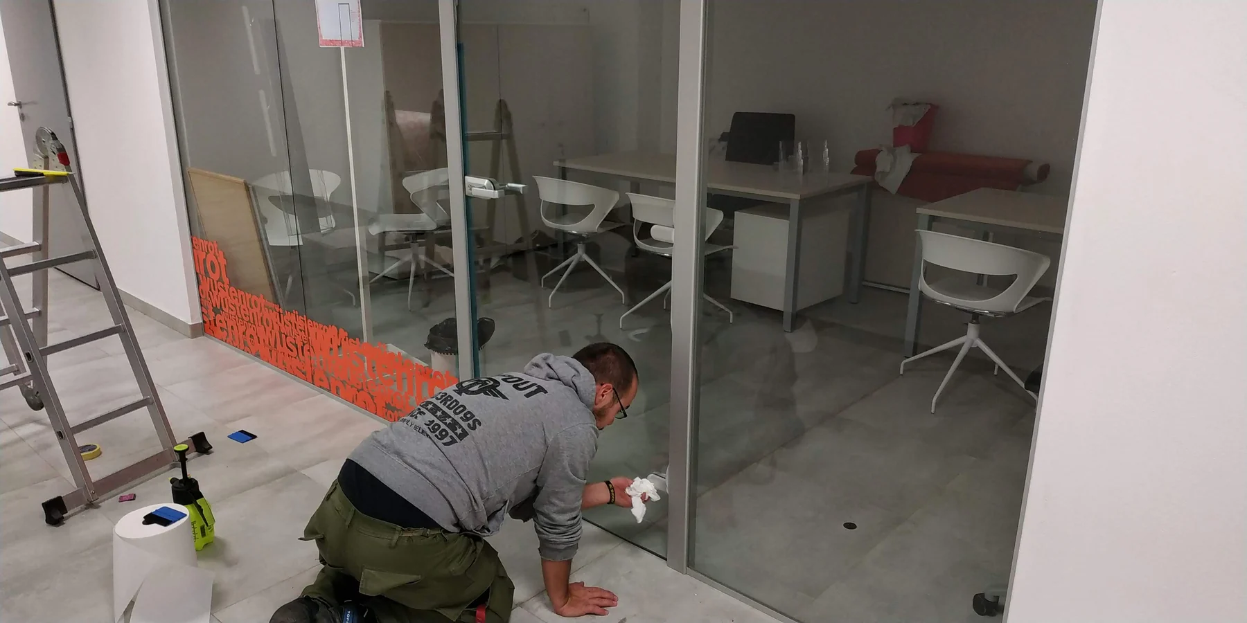 Aplikace oranžové grafiky na spodní část skleněné příčky